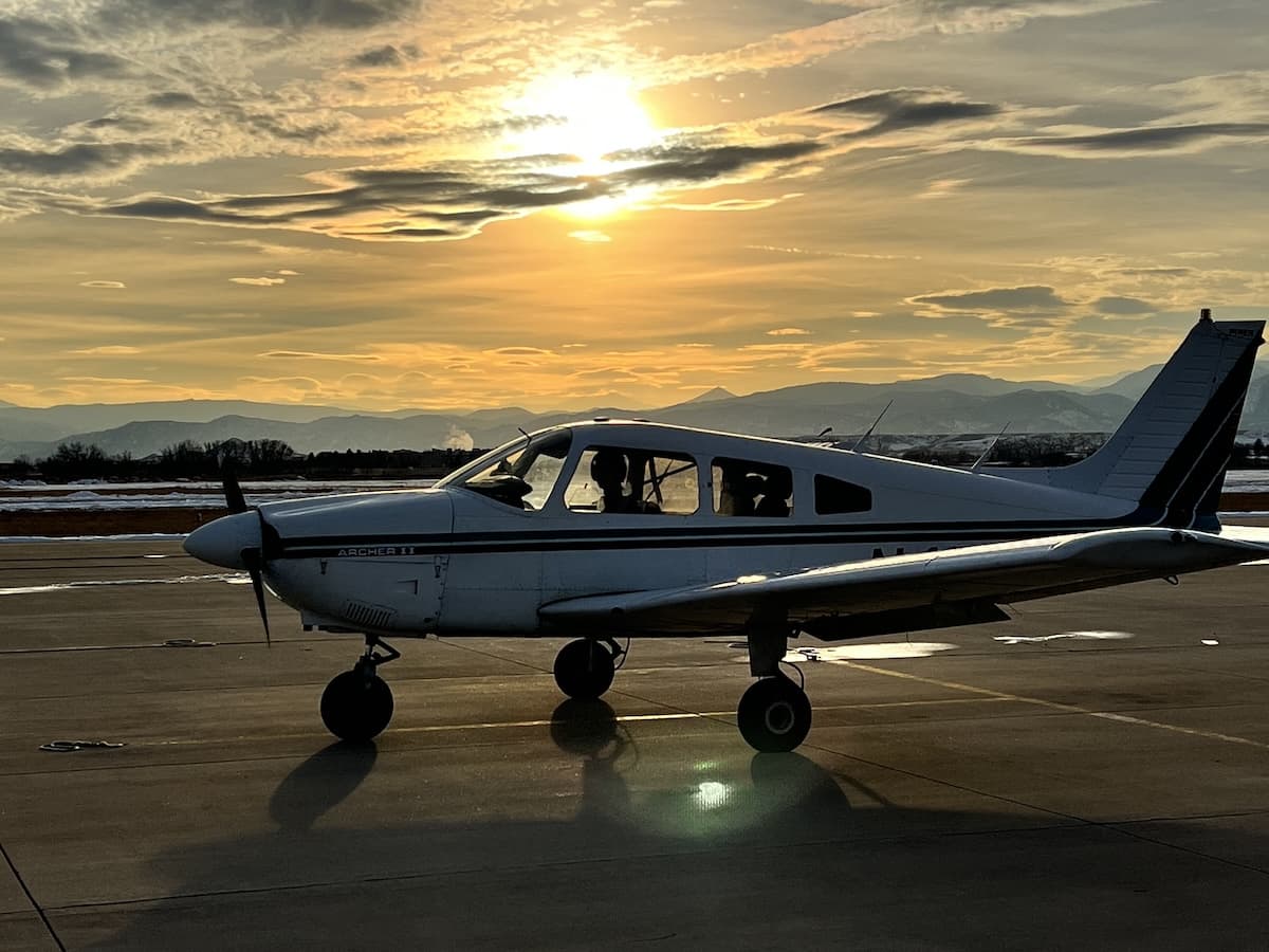 Student pilot's airplane at Vance Brand Airport KLMO after first solo flight with Rocky Mountains sunset backdrop.