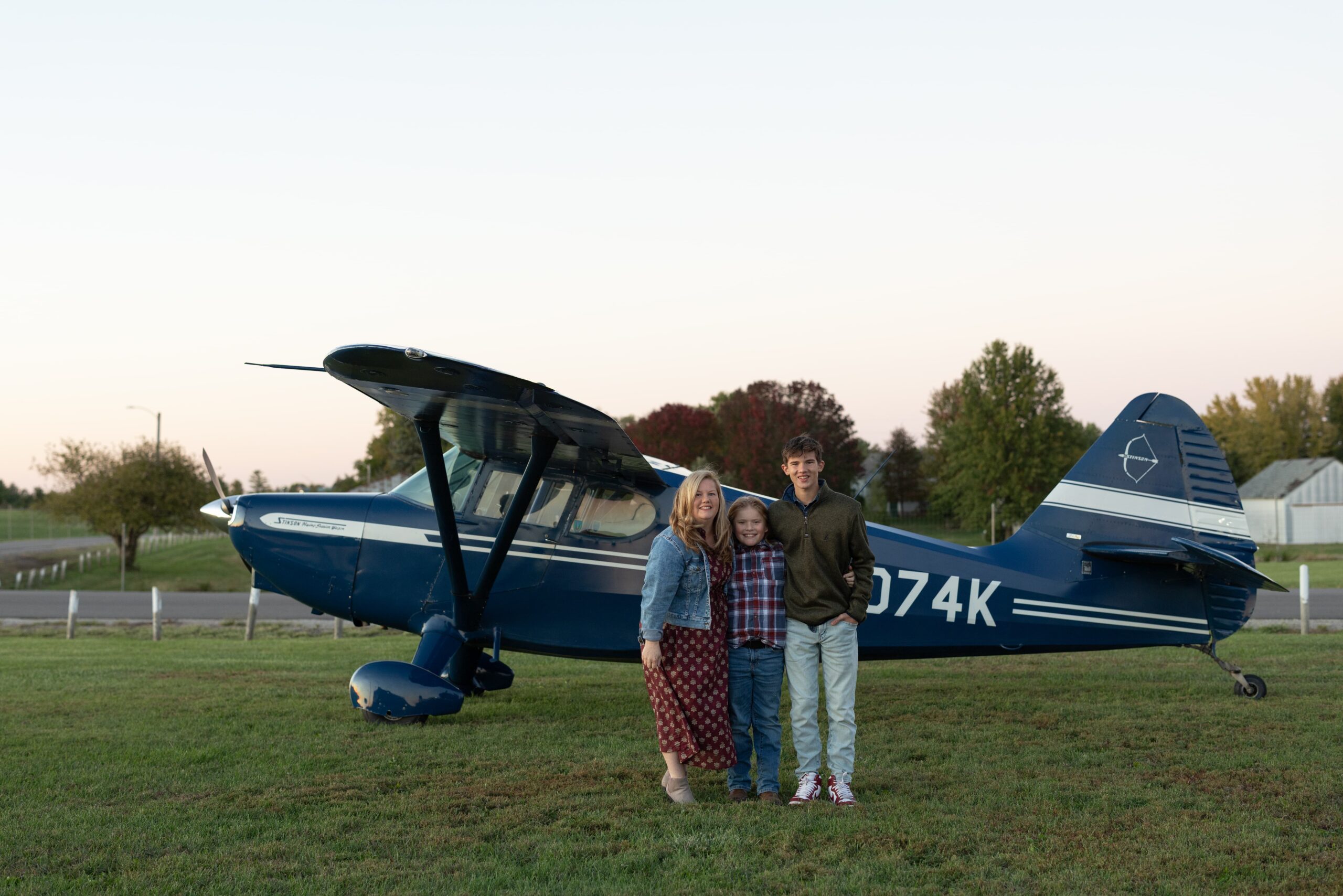 Megan Vandvoorde and her sons standing in front of their Stinson aircraft.
